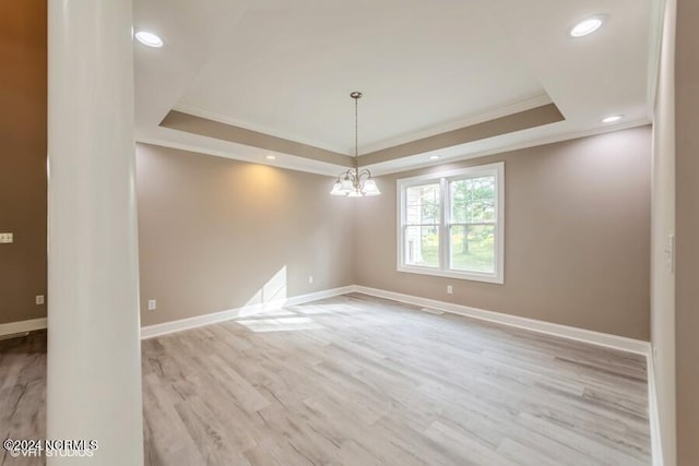 spare room with crown molding, a chandelier, light wood-type flooring, and a raised ceiling