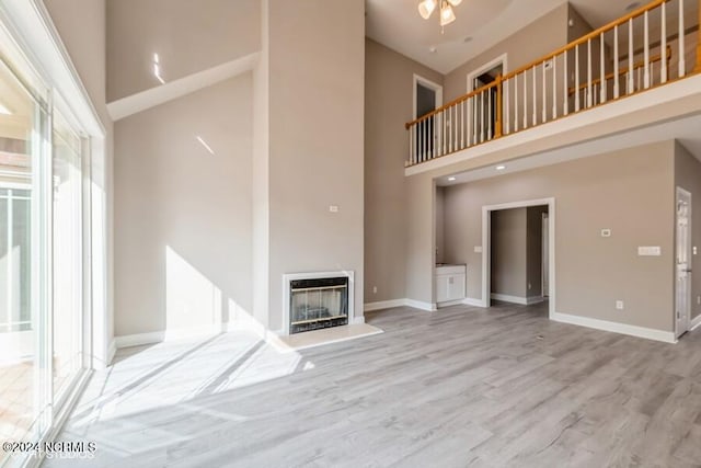 unfurnished living room with a high ceiling, light wood-type flooring, and ceiling fan