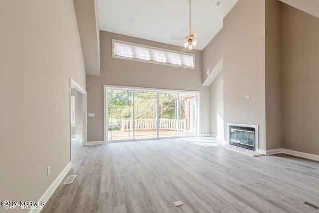 unfurnished living room with light hardwood / wood-style floors, high vaulted ceiling, and heating unit