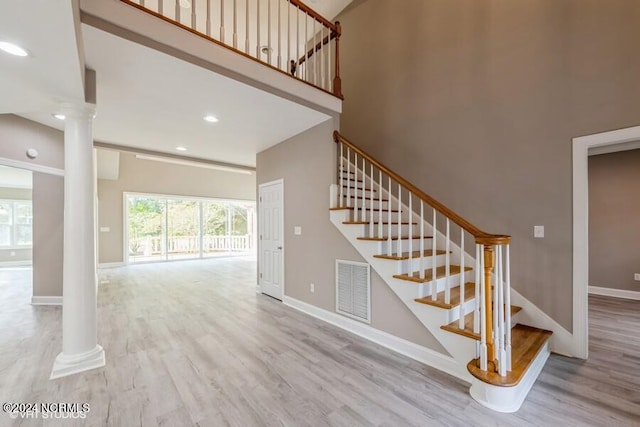 staircase featuring a towering ceiling, wood-type flooring, and decorative columns