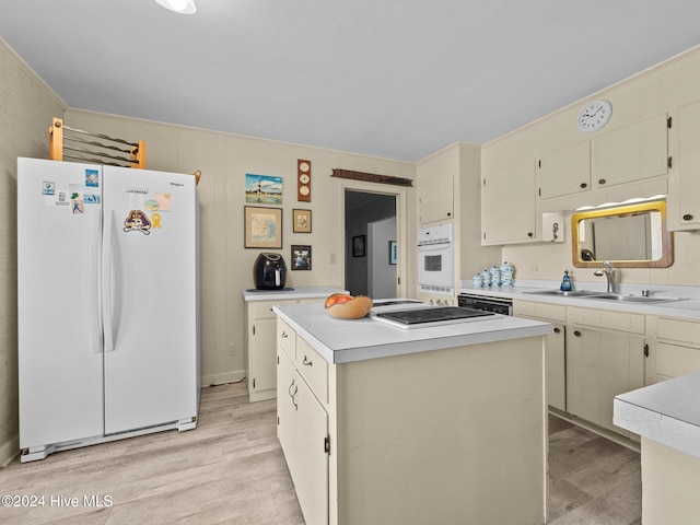 kitchen featuring a kitchen island, sink, white appliances, cream cabinetry, and light hardwood / wood-style flooring