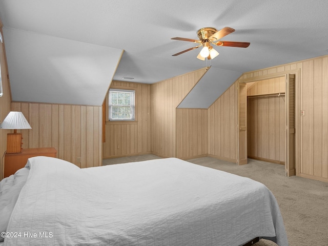 carpeted bedroom with ceiling fan, wooden walls, a closet, and vaulted ceiling