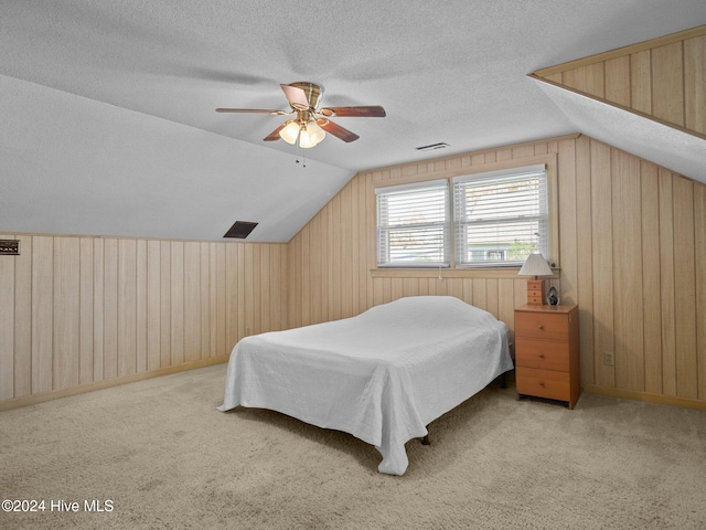 carpeted bedroom with wood walls, ceiling fan, a textured ceiling, and vaulted ceiling