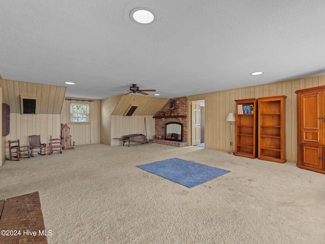 living room featuring carpet, a textured ceiling, ceiling fan, and a brick fireplace