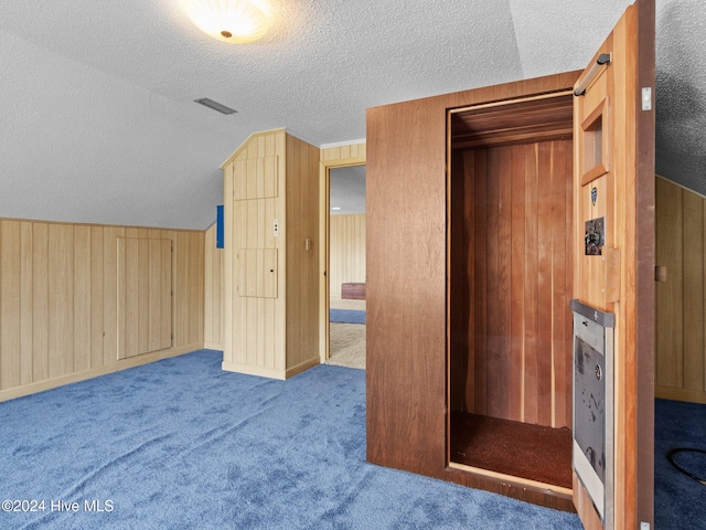 carpeted bedroom with wood walls, a textured ceiling, and vaulted ceiling