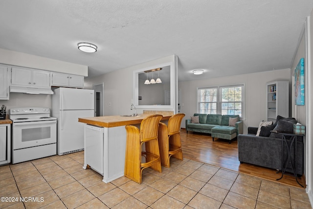 kitchen with white cabinets, a breakfast bar area, light wood-type flooring, decorative light fixtures, and white appliances