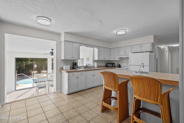 kitchen featuring tile counters, sink, a kitchen bar, white cabinetry, and white appliances