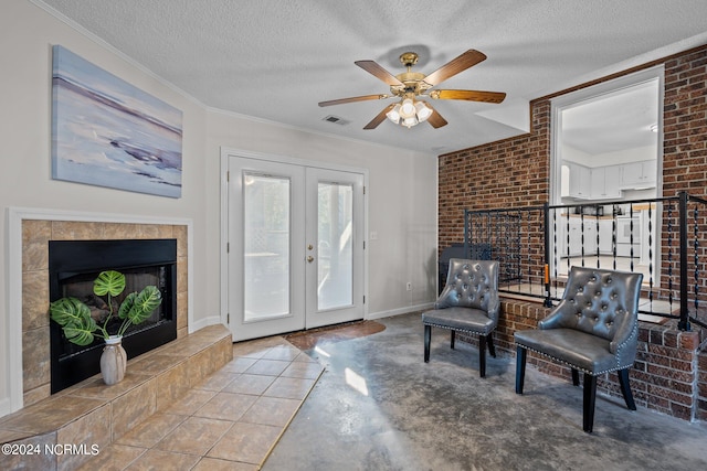 living area with french doors, a textured ceiling, ceiling fan, a tiled fireplace, and crown molding