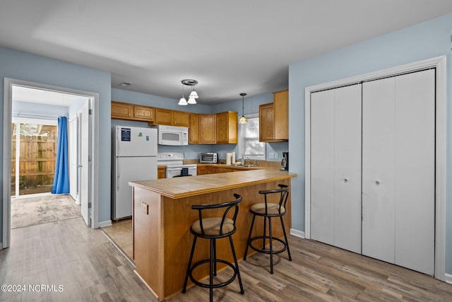 kitchen featuring kitchen peninsula, light hardwood / wood-style flooring, sink, decorative light fixtures, and white appliances