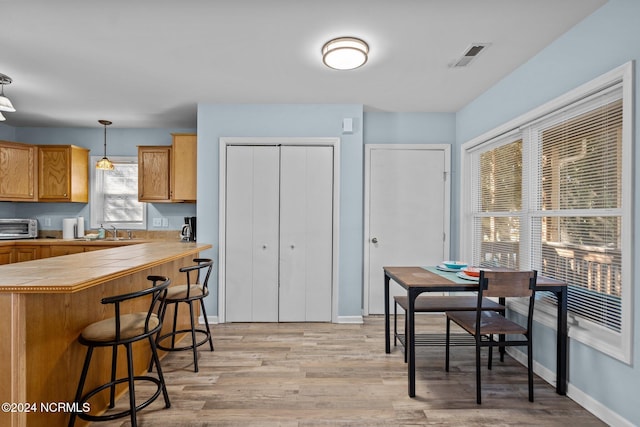 kitchen featuring sink, a kitchen breakfast bar, pendant lighting, and light wood-type flooring