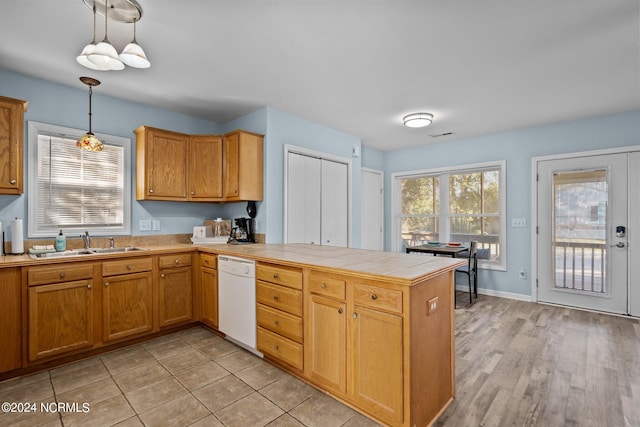 kitchen with sink, white dishwasher, hanging light fixtures, light hardwood / wood-style floors, and tile counters