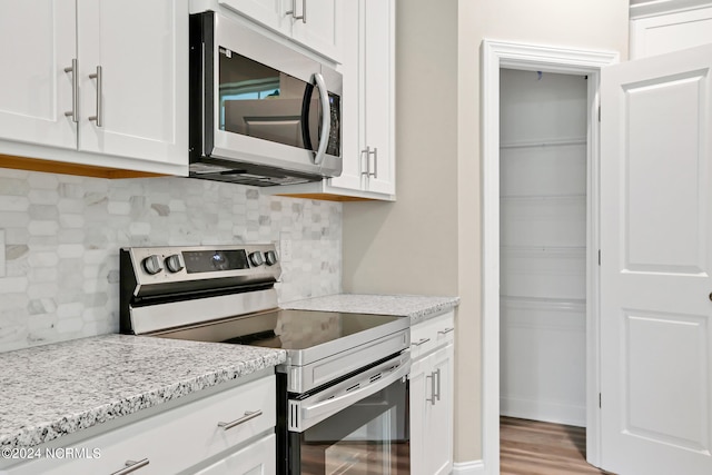 kitchen with appliances with stainless steel finishes, white cabinets, light stone counters, and backsplash