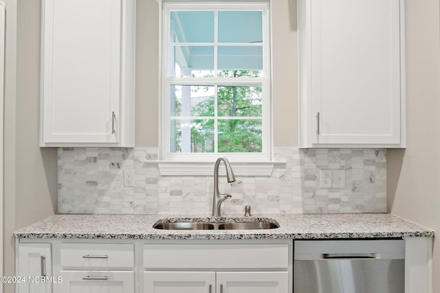 kitchen with stainless steel dishwasher, white cabinetry, light stone countertops, and sink