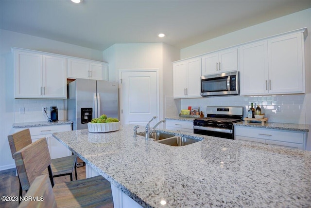 kitchen featuring a kitchen breakfast bar, sink, white cabinets, appliances with stainless steel finishes, and light stone counters