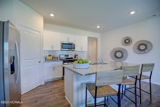 kitchen featuring appliances with stainless steel finishes, white cabinetry, dark wood-type flooring, a breakfast bar, and a kitchen island with sink