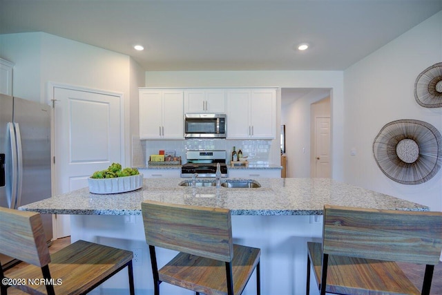 kitchen with appliances with stainless steel finishes, white cabinetry, a center island with sink, and a kitchen bar