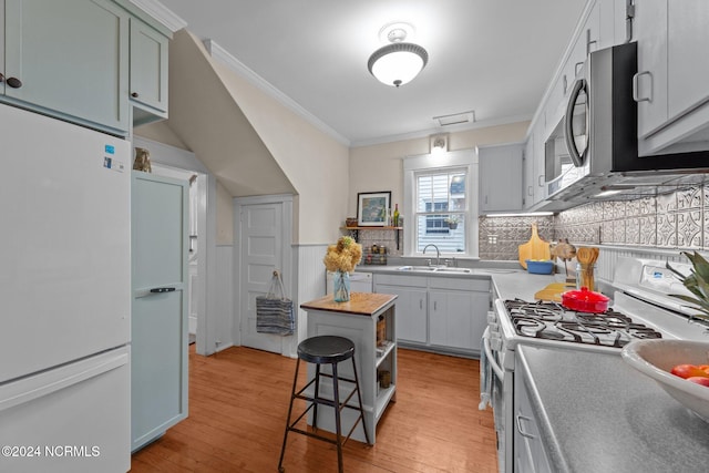 kitchen with sink, white appliances, a kitchen bar, ornamental molding, and light wood-type flooring