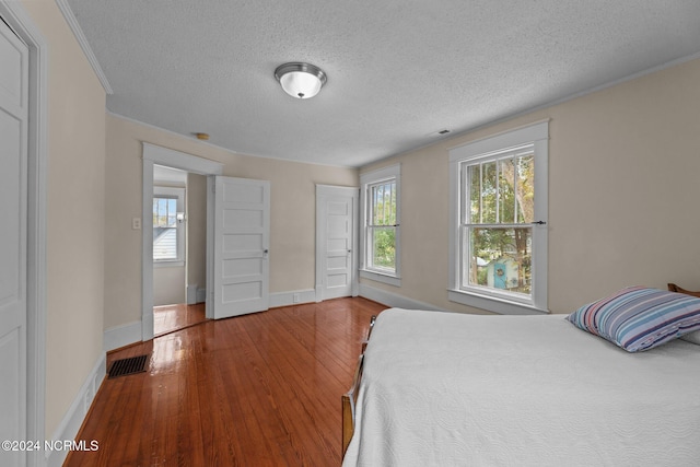 bedroom featuring a textured ceiling, crown molding, multiple windows, and hardwood / wood-style flooring