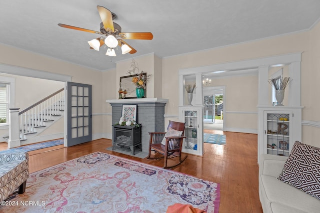 living room with a wood stove, ceiling fan with notable chandelier, and hardwood / wood-style flooring