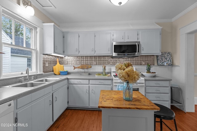 kitchen featuring white appliances, wood-type flooring, crown molding, a kitchen bar, and sink