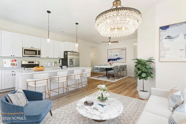 living room featuring light hardwood / wood-style floors, sink, and ceiling fan with notable chandelier