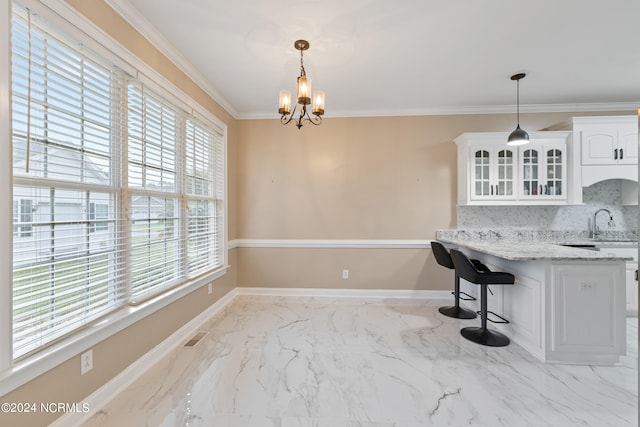 kitchen with an inviting chandelier, white cabinetry, light stone countertops, ornamental molding, and decorative light fixtures