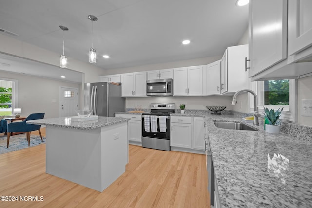 kitchen with white cabinets, appliances with stainless steel finishes, light stone countertops, light hardwood / wood-style flooring, and sink