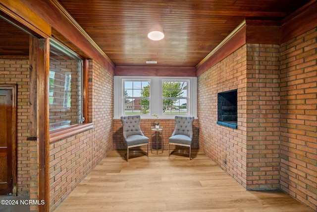 sitting room with brick wall, light hardwood / wood-style flooring, ornamental molding, and wooden ceiling