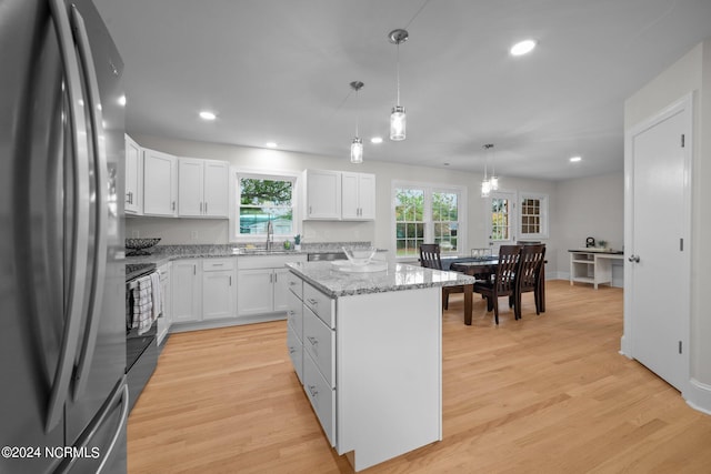 kitchen with white cabinetry, stainless steel refrigerator, light hardwood / wood-style floors, decorative light fixtures, and a center island