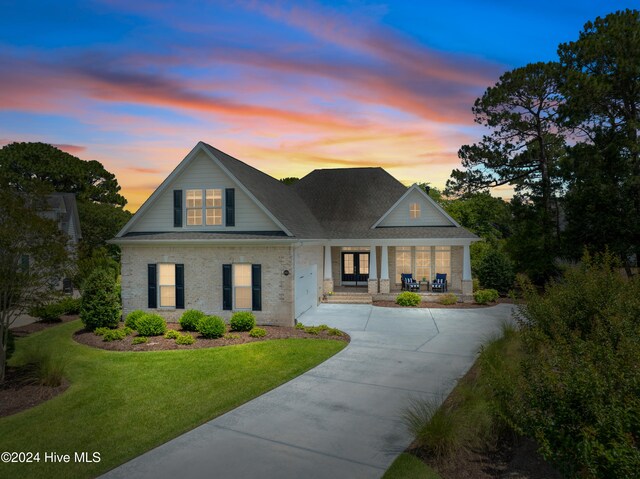 view of front of house featuring brick siding, an attached garage, a front lawn, covered porch, and driveway