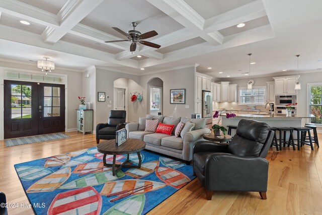 living area featuring beam ceiling, arched walkways, light wood-type flooring, and ornamental molding