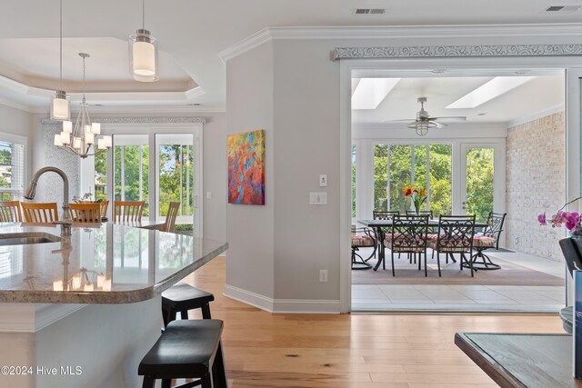 kitchen featuring visible vents, light wood-type flooring, a tray ceiling, ornamental molding, and a sink