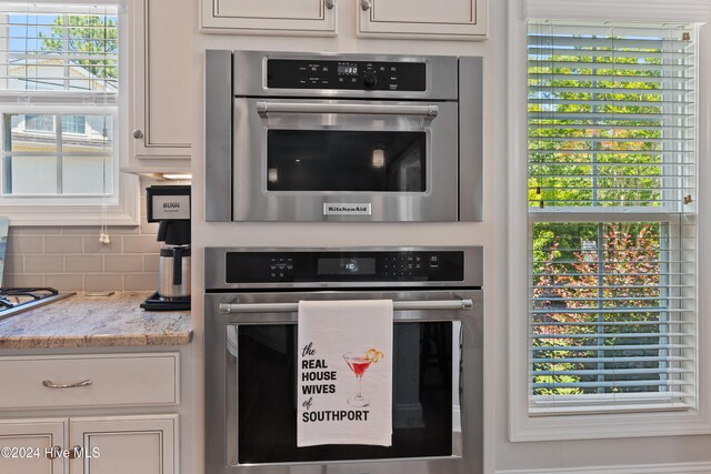 kitchen featuring stainless steel oven, decorative backsplash, light stone counters, and white cabinets