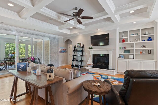 living area with ornamental molding, beam ceiling, a premium fireplace, light wood-style floors, and arched walkways