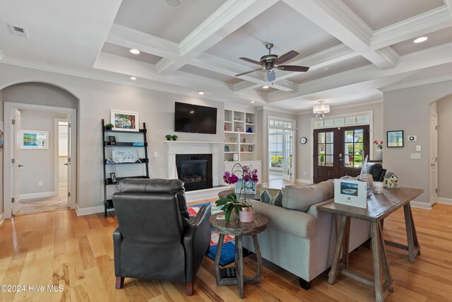 living area featuring visible vents, beamed ceiling, coffered ceiling, arched walkways, and light wood finished floors