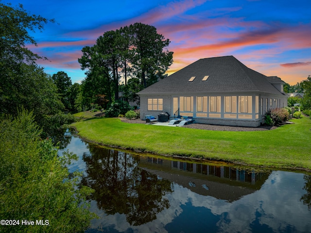 back of house with a lawn, roof with shingles, a patio, and a water view