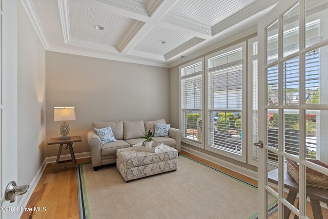 living room featuring light wood-style floors, coffered ceiling, a healthy amount of sunlight, and ornamental molding