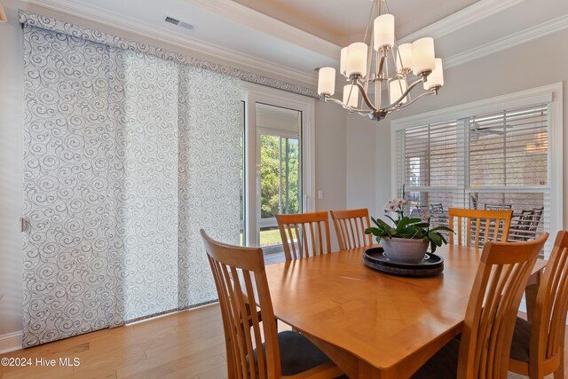 dining room featuring visible vents, a tray ceiling, ornamental molding, an inviting chandelier, and wood finished floors