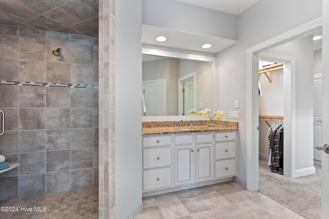 full bathroom featuring recessed lighting, tiled shower, vanity, baseboards, and a spacious closet