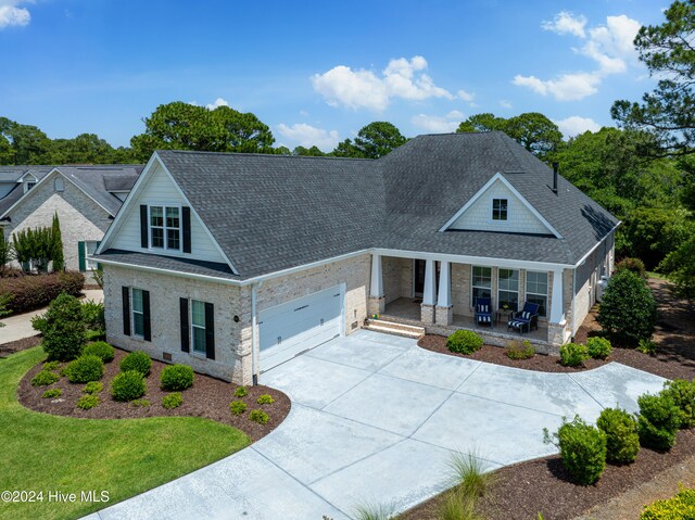 craftsman-style home featuring covered porch, a shingled roof, concrete driveway, a front lawn, and a garage