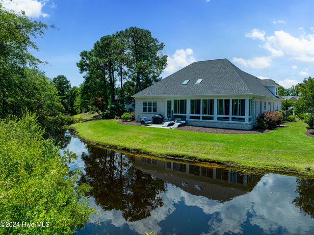 rear view of property with a yard, a water view, roof with shingles, and a patio area