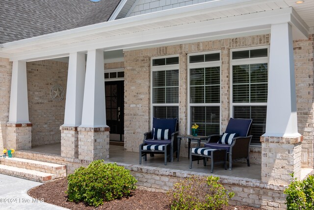 entrance to property with brick siding, covered porch, and a shingled roof