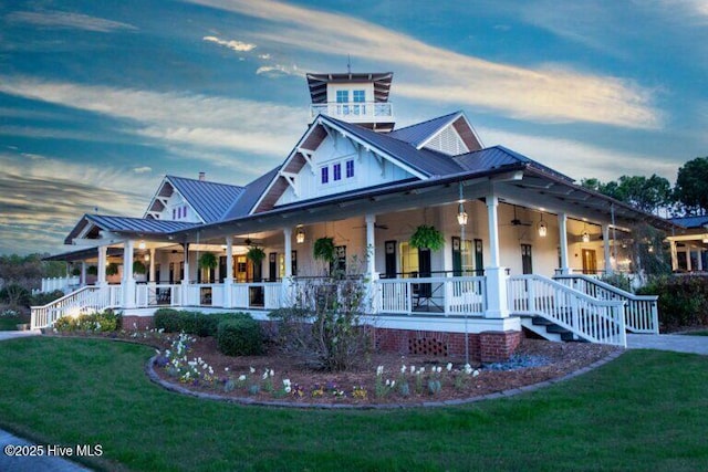 farmhouse-style home with a front yard, covered porch, metal roof, a ceiling fan, and a standing seam roof