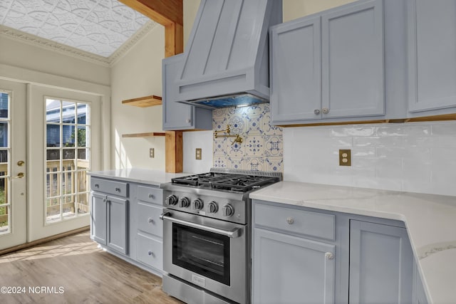 kitchen featuring light wood-type flooring, premium range hood, light stone counters, ornamental molding, and stainless steel stove