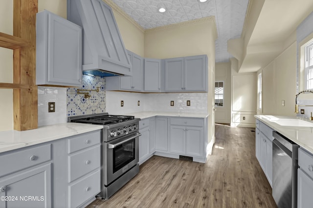 kitchen featuring sink, stainless steel appliances, light hardwood / wood-style floors, custom range hood, and ornamental molding