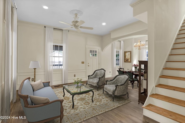 living room with ceiling fan with notable chandelier, light hardwood / wood-style flooring, and crown molding