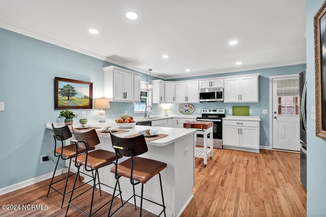 kitchen with appliances with stainless steel finishes, sink, light hardwood / wood-style floors, pendant lighting, and white cabinets