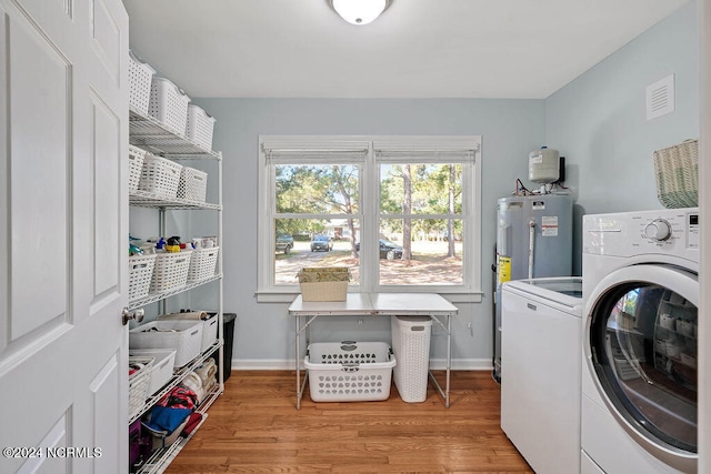 clothes washing area with light hardwood / wood-style flooring, water heater, and separate washer and dryer