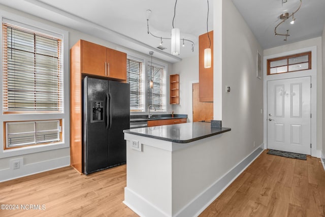 kitchen featuring black fridge, kitchen peninsula, hanging light fixtures, sink, and light hardwood / wood-style floors