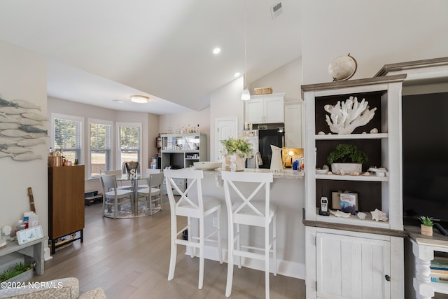 kitchen featuring lofted ceiling, white cabinets, a breakfast bar area, black fridge, and dark wood-type flooring